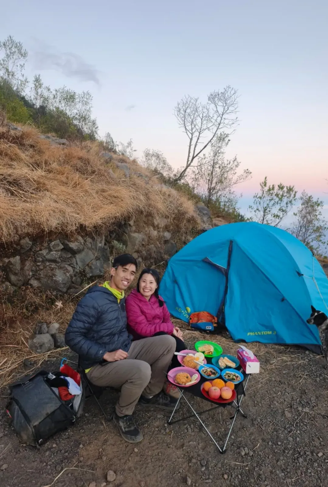 Trekkers sharing a meal beside a blue tent on Mount Agung