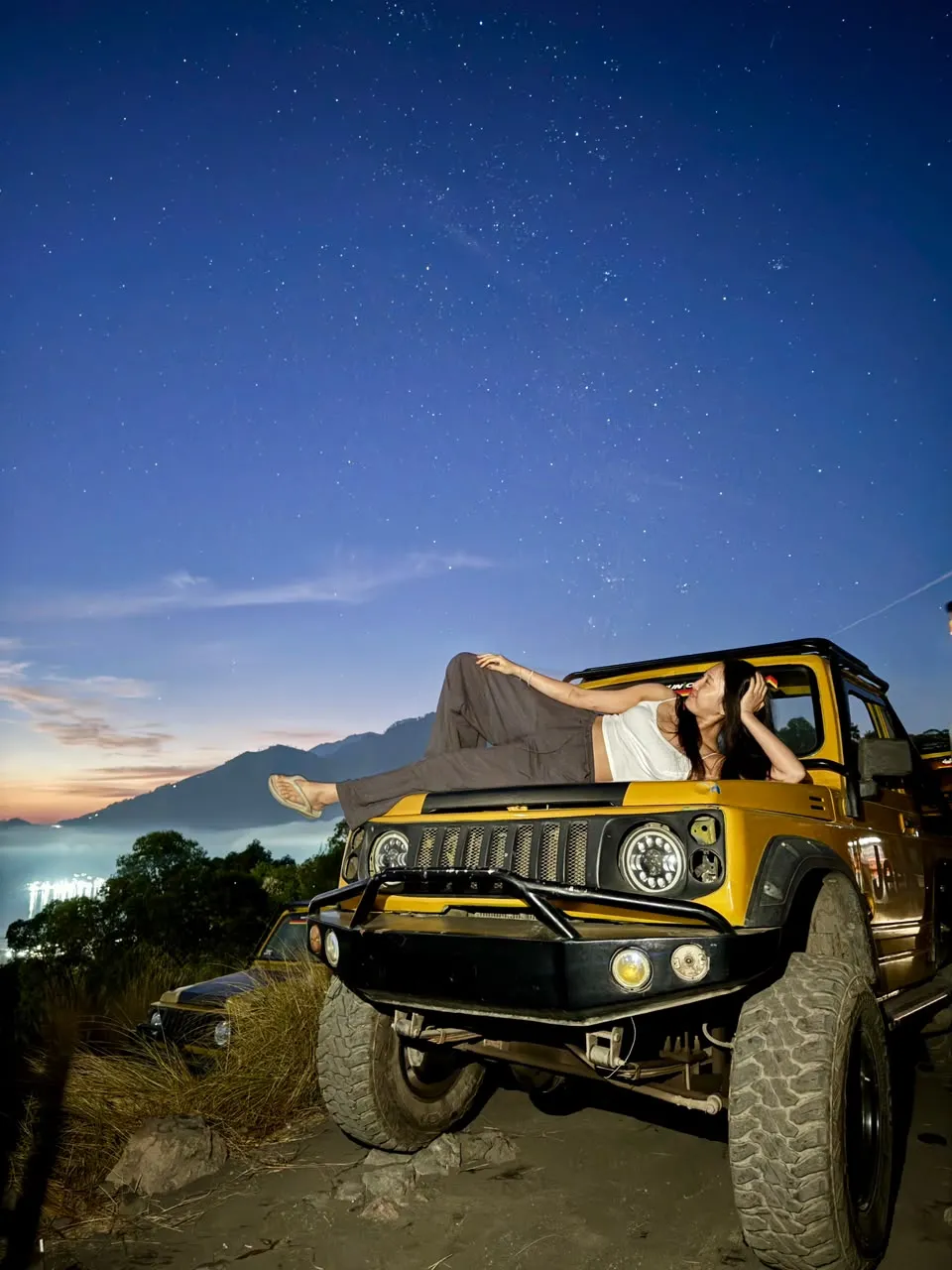 Guest resting on the yellow jeep under a starry pre-dawn sky