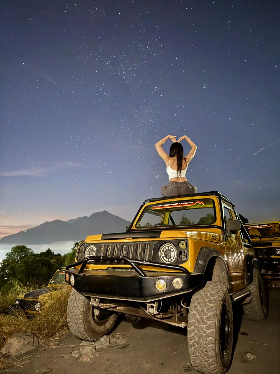 Guest on the yellow jeep roof under a sky full of stars