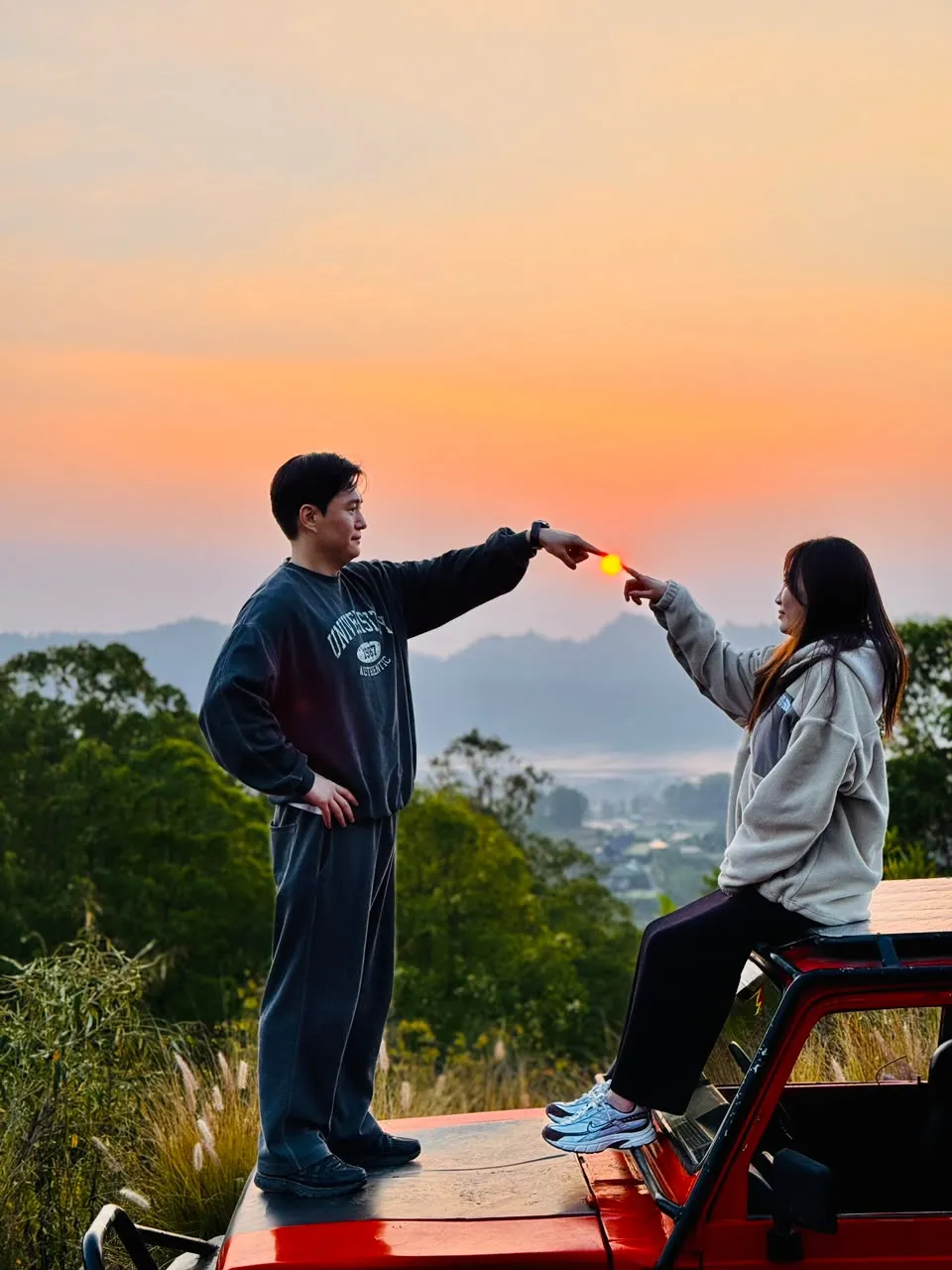 Two guests framing the sunrise from the red jeep
