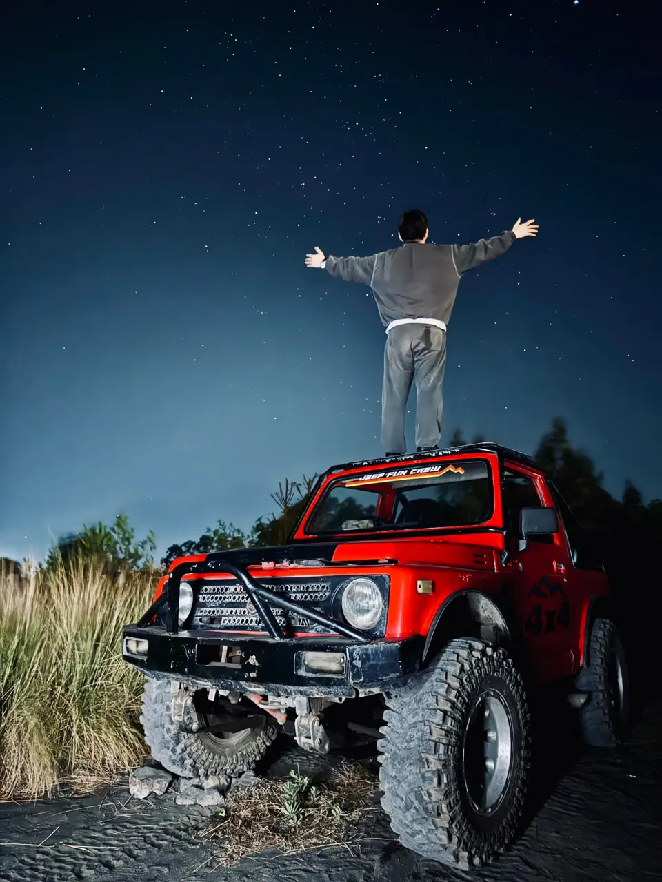 Guest standing on the red jeep under the night sky