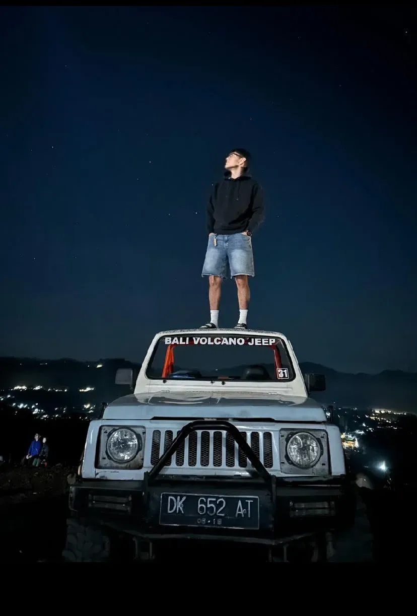 Guest standing on a white jeep under a night sky above village lights