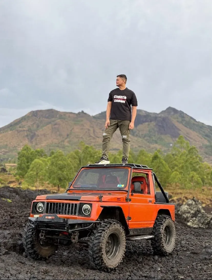 Guest standing on an orange jeep on a black lava field with Mount Batur behind