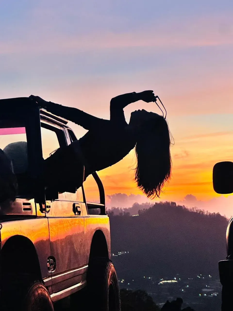Silhouette of a guest leaning from a jeep against an orange sky