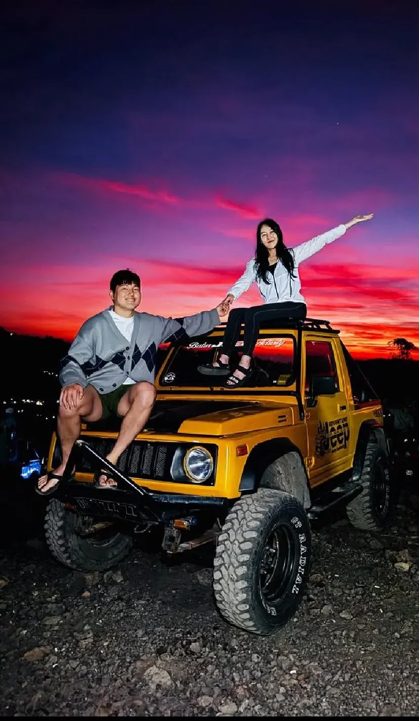Two guests on a yellow jeep under a red and purple dawn sky