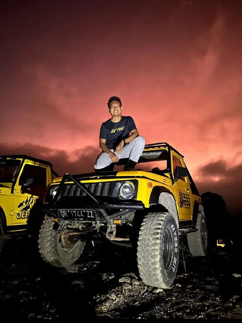 Guest seated on a yellow jeep under a red morning sky
