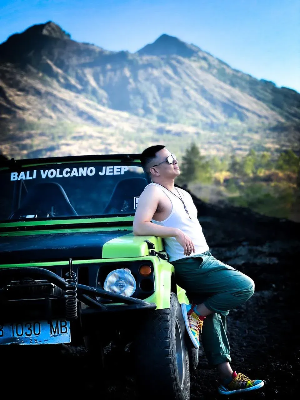 Guest leaning on a green jeep with Mount Batur’s slopes behind