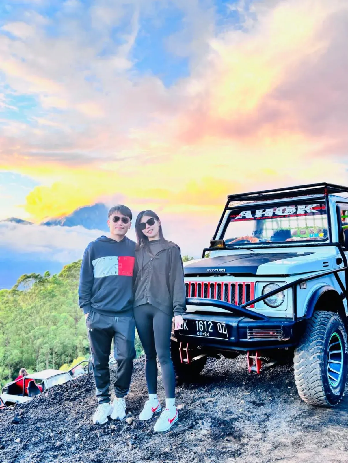 Two guests beside a white jeep on black volcanic ground at sunrise