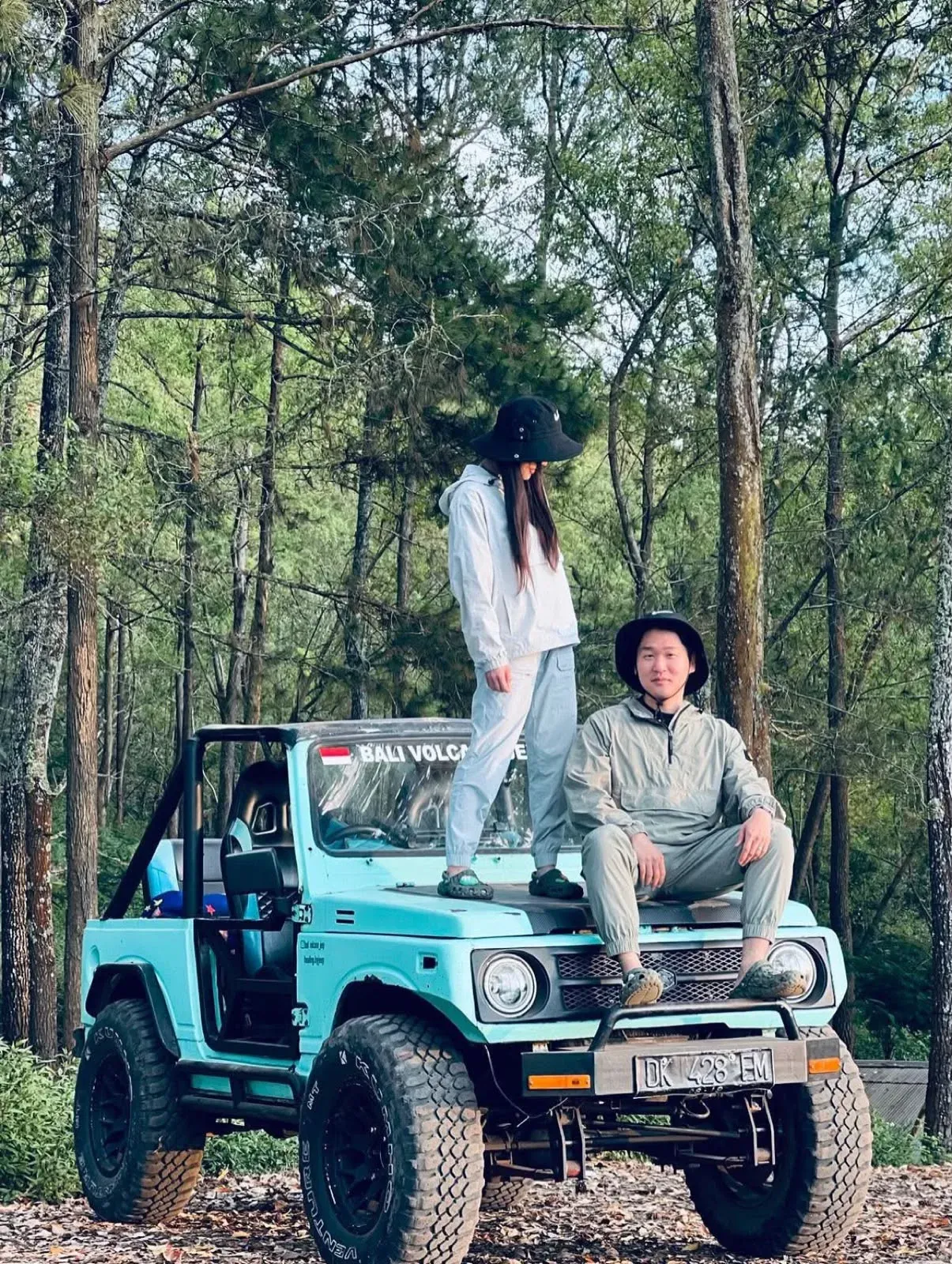 Two guests with a turquoise jeep in a pine forest
