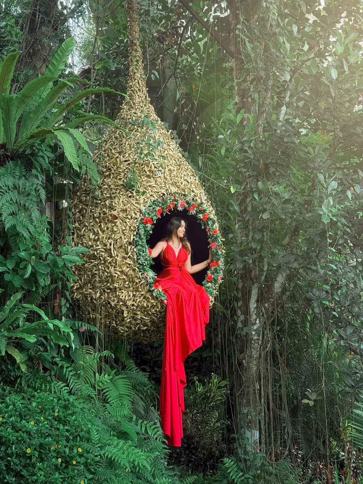 A woman in a red dress seated in a woven nest hung among the trees at Alas Harum