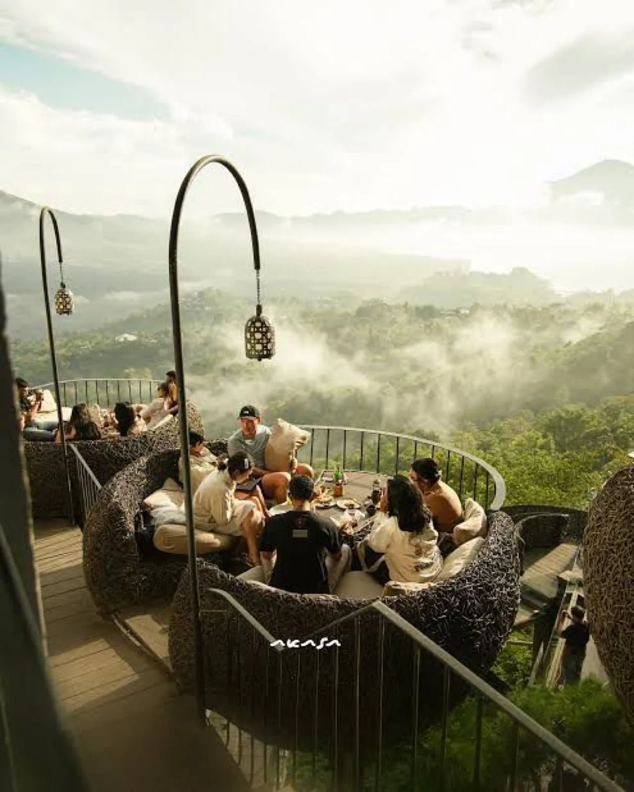 Guests on curved sofas above a misty valley, with the name Akasa on the rail