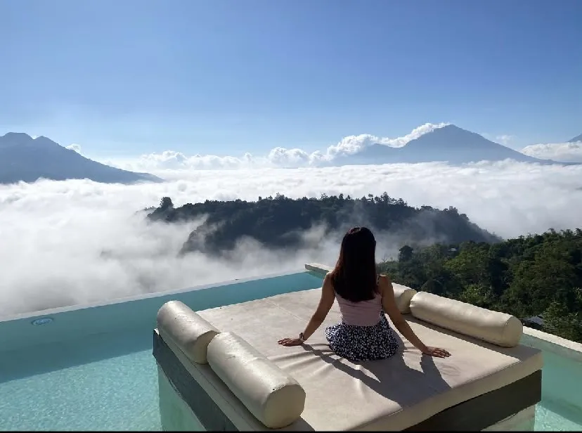 A guest on a daybed above a sea of cloud, with volcanoes beyond
