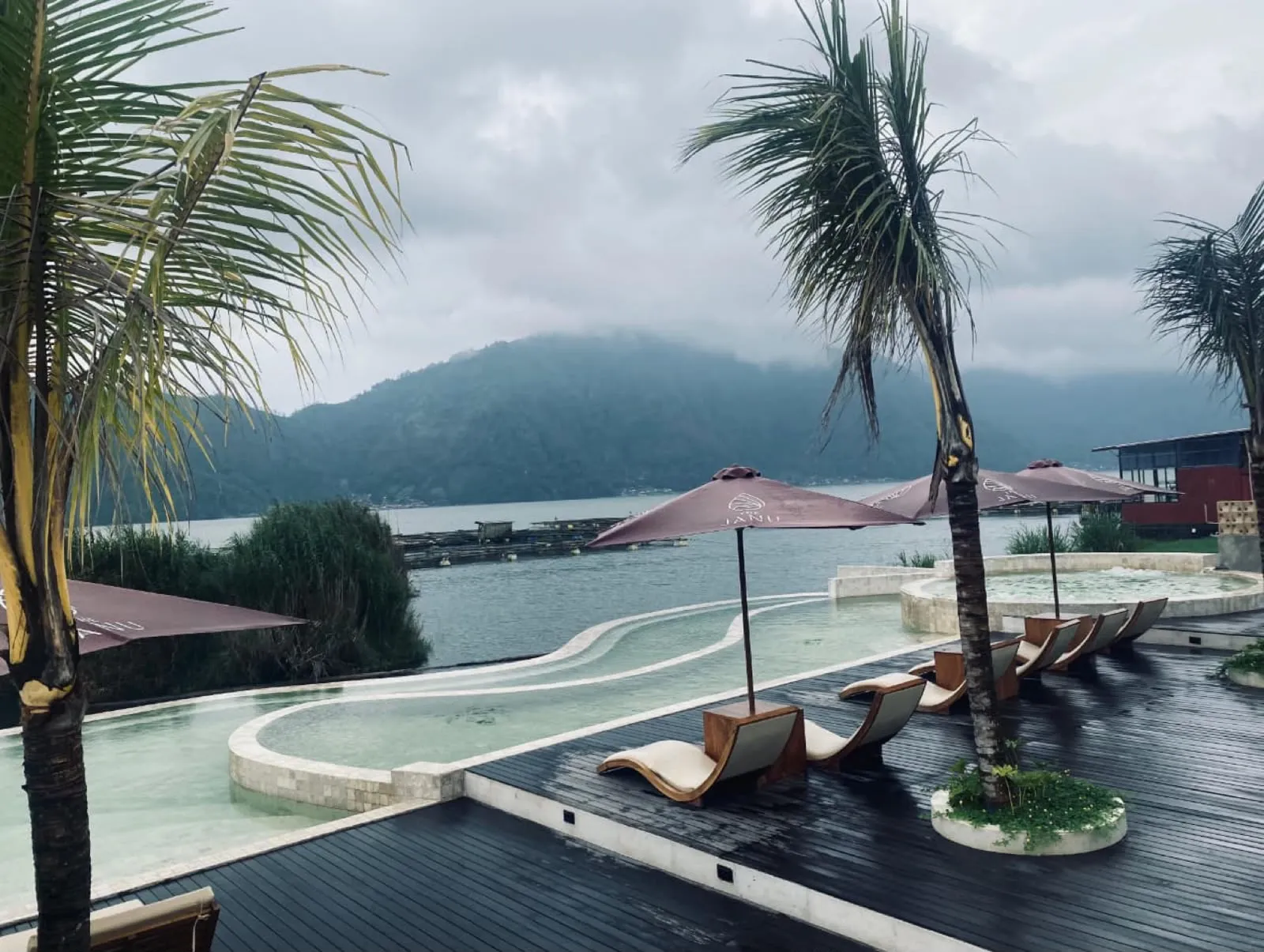 Infinity pools and a round hot tub beside a lake, with a Janu umbrella over the deck