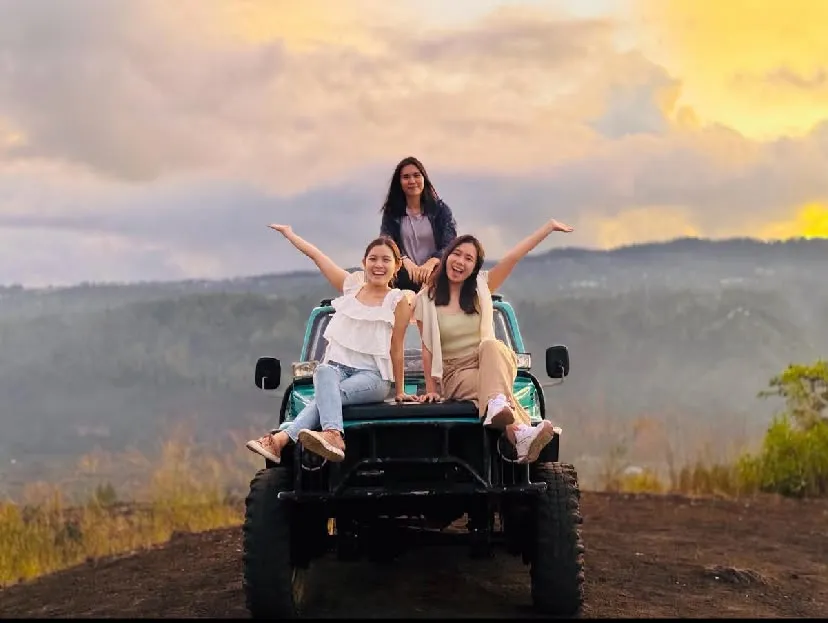 Three guests posing on a turquoise 4WD jeep on a ridge at sunset