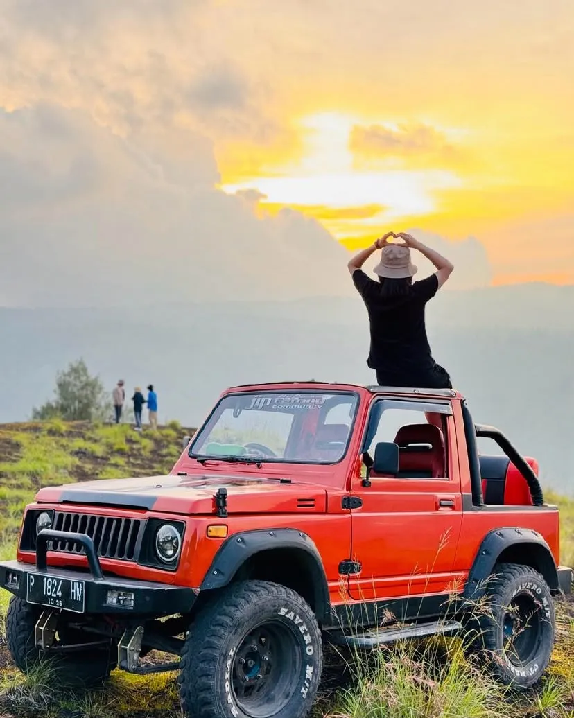 Guest making a heart shape on a red jeep as the sun sets over the ridge
