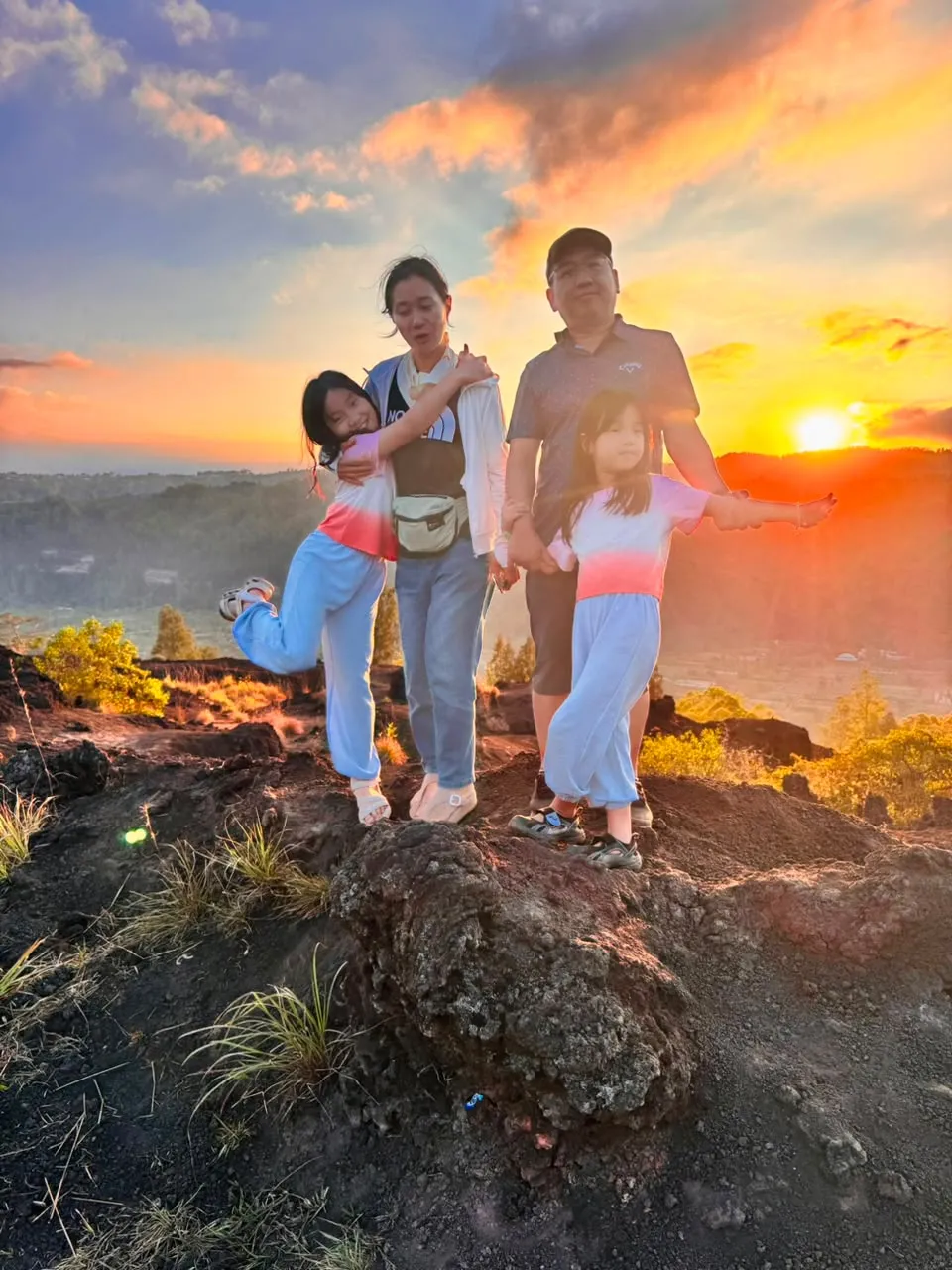 A family standing on volcanic rock with the sun on the horizon
