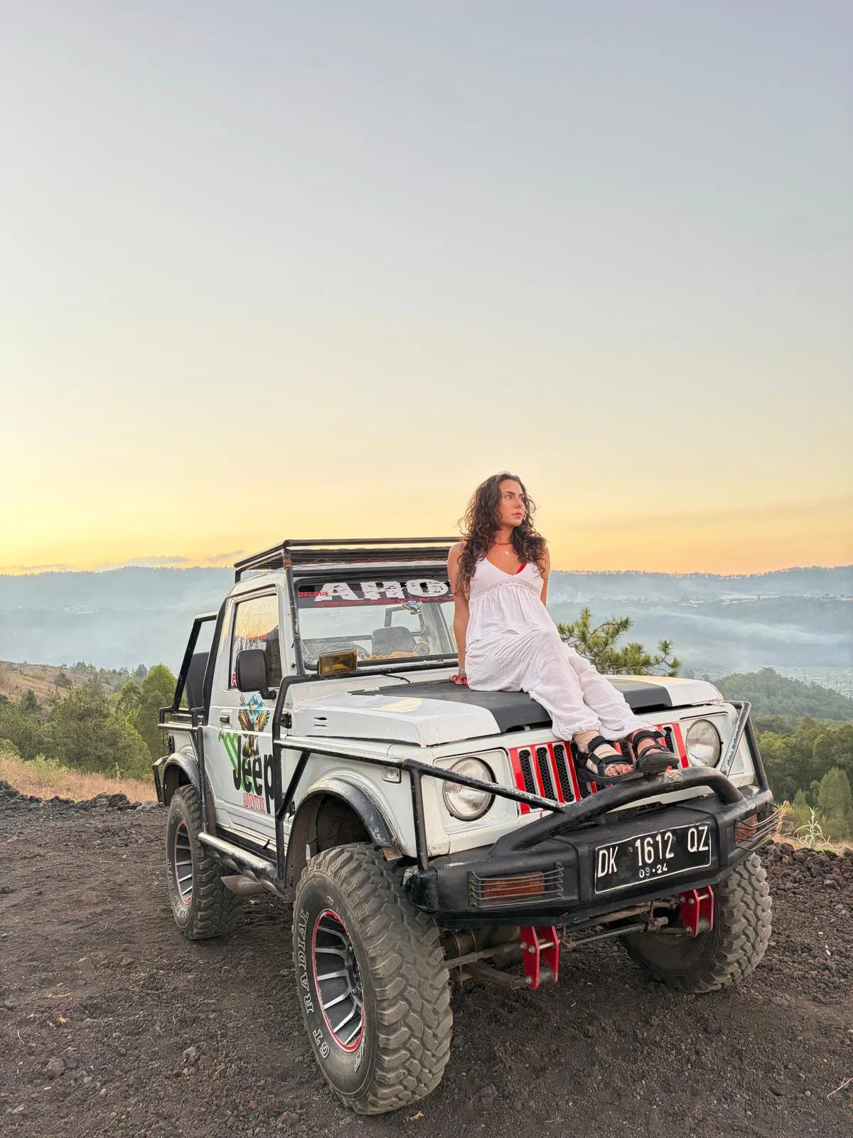Guest in white seated on a white jeep above the valley as the sky turns gold