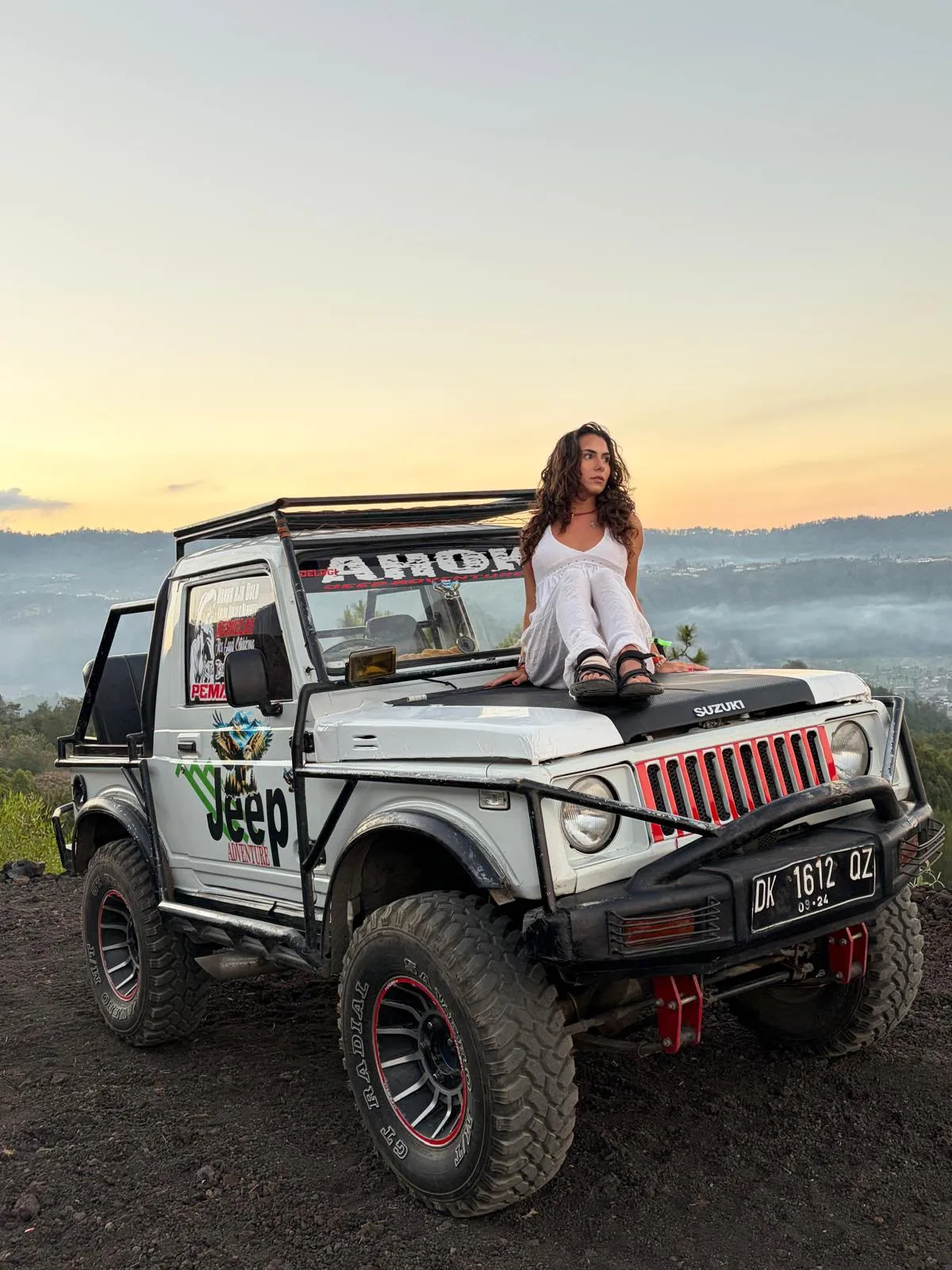 Guest seated on a white jeep above a valley at dusk