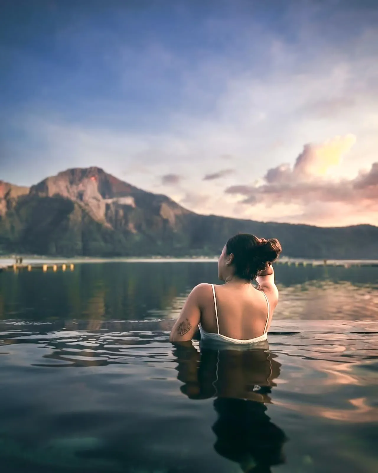 Guest in a lakeside pool facing a Bali mountain