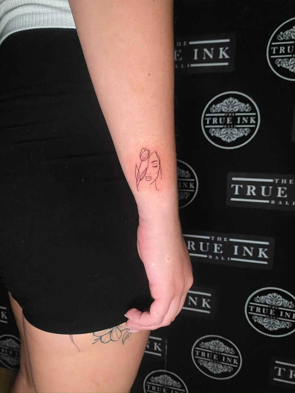 Small fine-line tulip and face on the inner wrist at The True Ink Bali