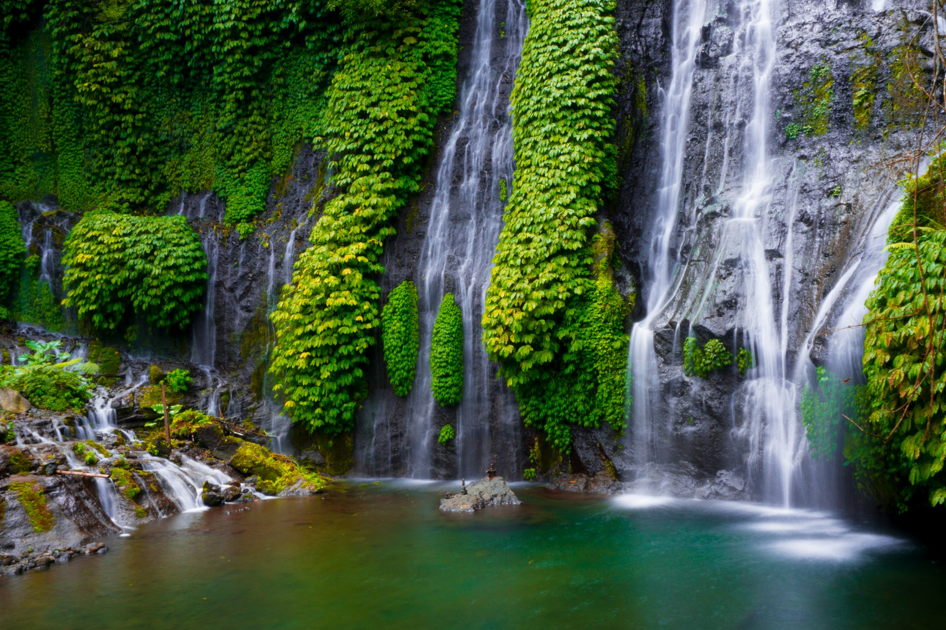 Tall jungle waterfall falling into a green pool in North Bali