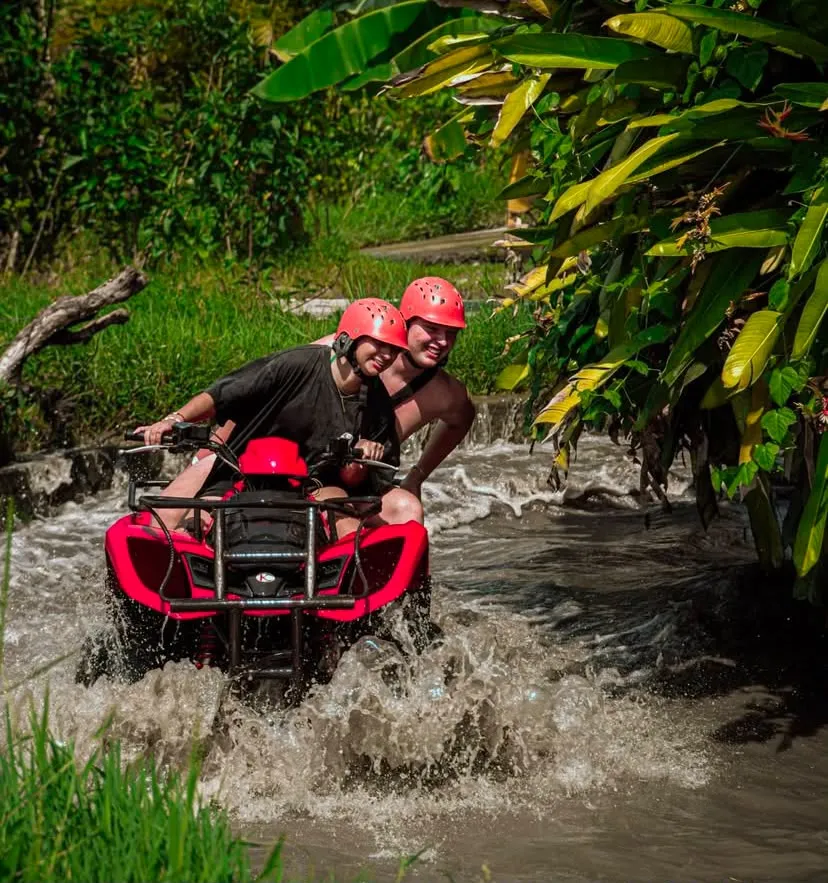 Couple riding an ATV through a jungle water crossing