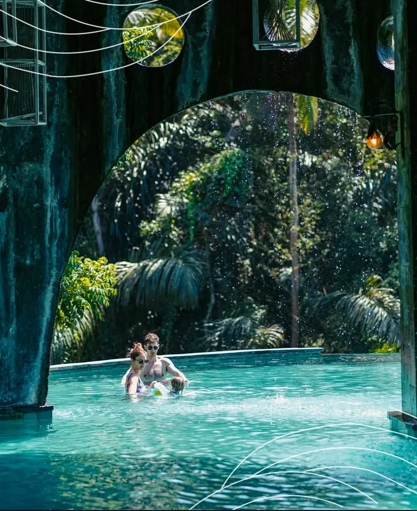 Family swimming under a stone arch at Tlaga Singha