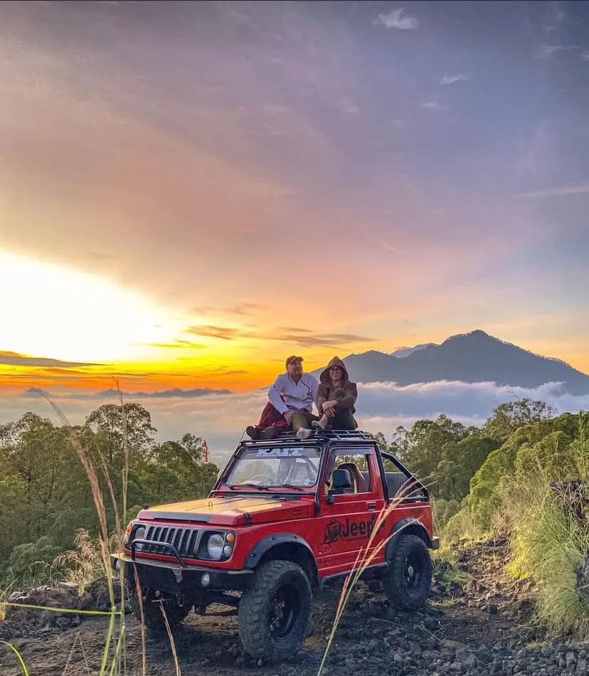 Couple sitting on a red jeep at sunrise above the clouds