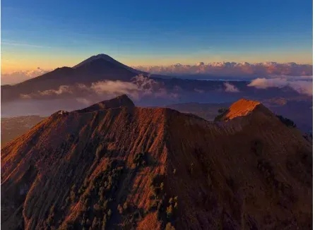 Mount Batur ridges in warm sunrise light, with a neighboring peak beyond the clouds