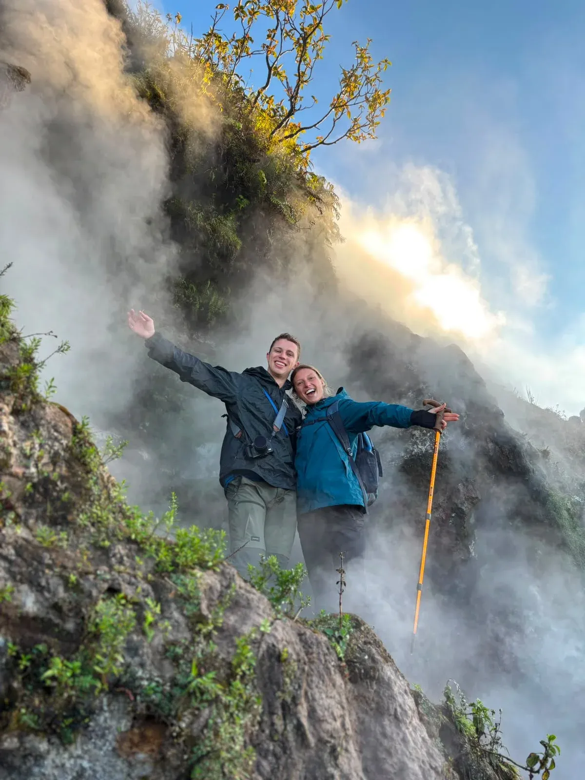 Two trekkers on a rocky Mount Batur trail in morning steam, one holding a trekking pole