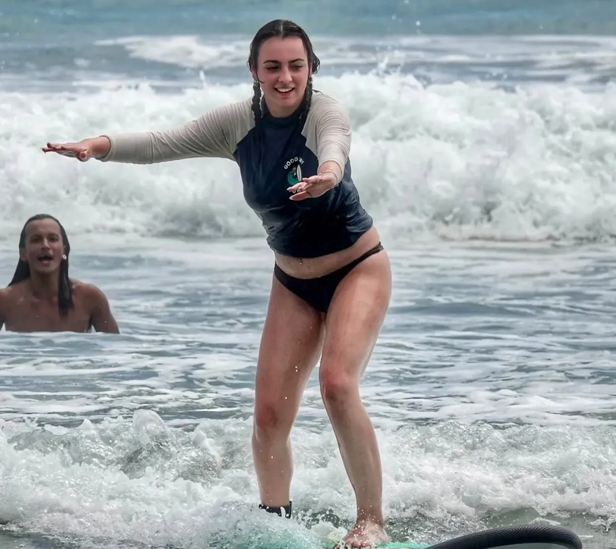 A student standing on a board in the whitewater with an instructor beside them