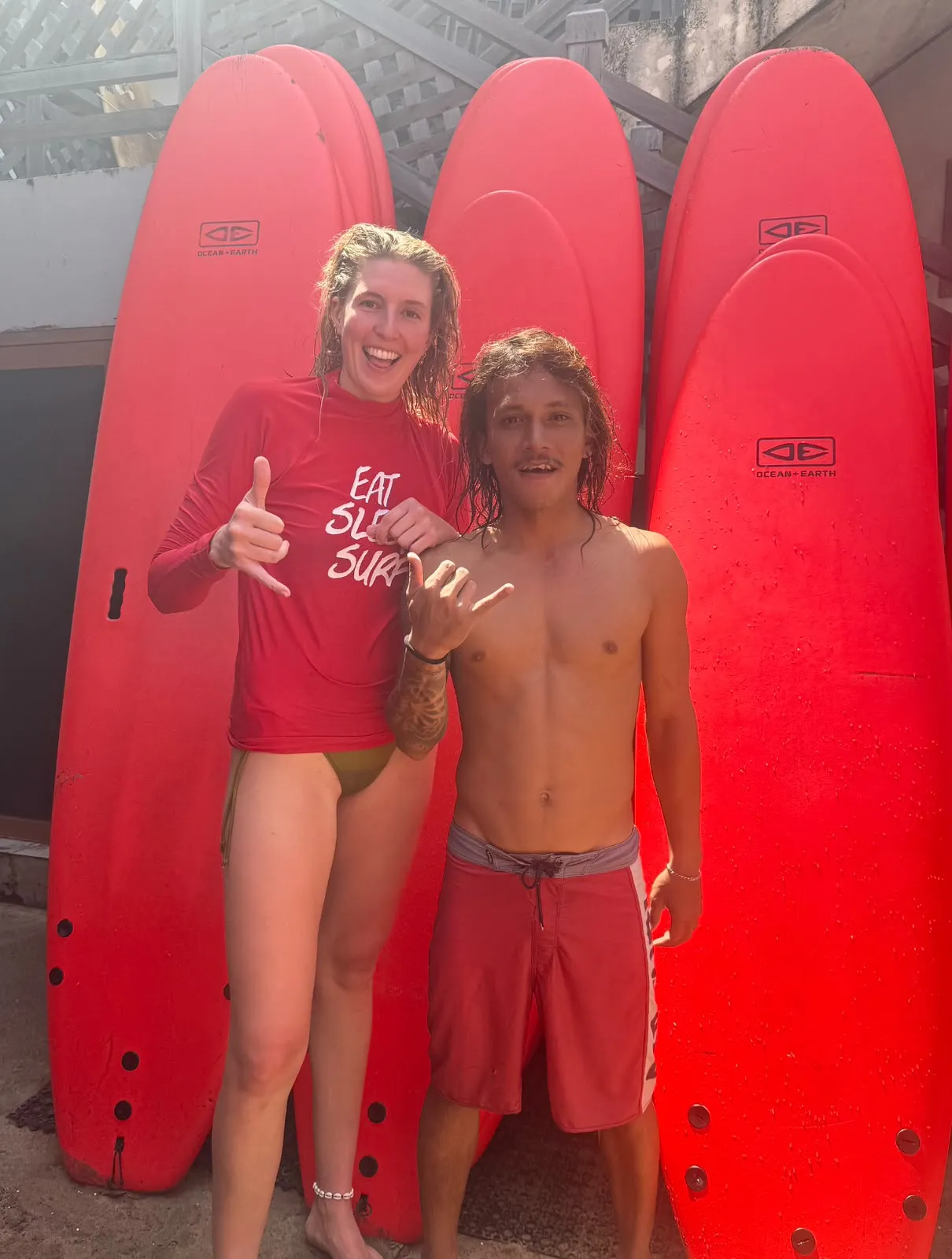 Two surfers standing in front of a rack of red boards