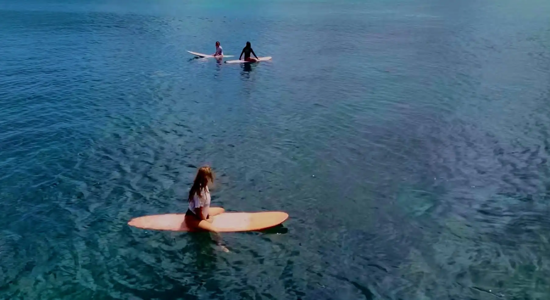 Three surfers sitting on boards in clear blue water